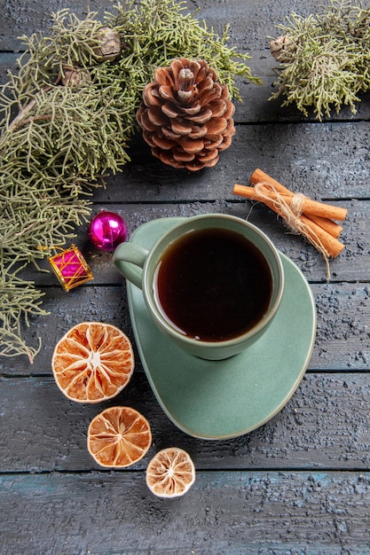 Vista superior de una taza de té ramas de abeto juguetes navideños naranjas secas canela en mesa de madera oscura