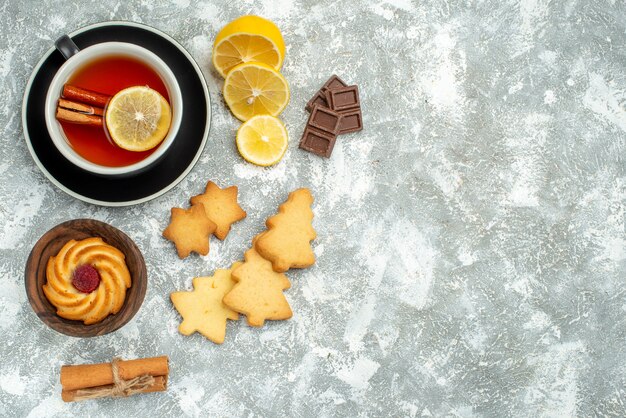 Vista superior de una taza de té, rodajas de limón, canela, chocolates, galletas en la superficie gris lugar libre