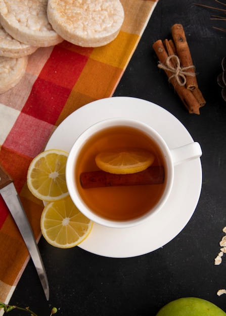 Vista superior taza de té con rodajas de limón y canela con un cuchillo sobre la mesa