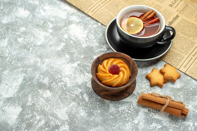 Vista superior de una taza de té con rodajas de limón y canela en galletas de periódico en el lugar de copia de superficie gris