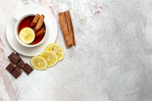 Vista superior de la taza de té con rodajas de limón y chocolate sobre superficie blanca