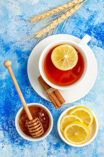 Vista superior de la taza de té con rodajas de limón miel canela en mesa azul