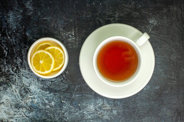 Vista superior de la taza de té de rodajas de limón en un platillo pequeño en la mesa oscura