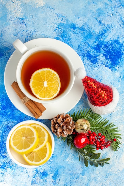 Vista superior de una taza de té, rodajas de limón, rama de árbol de Navidad, gorro de Papá Noel en la mesa azul