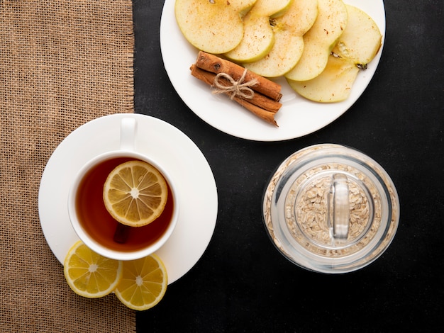 Vista superior taza de té con rodajas de limón y rodajas de manzana con canela en un plato