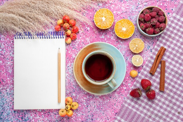 Vista superior de la taza de té con rodajas de naranja y frambuesas en la superficie rosa