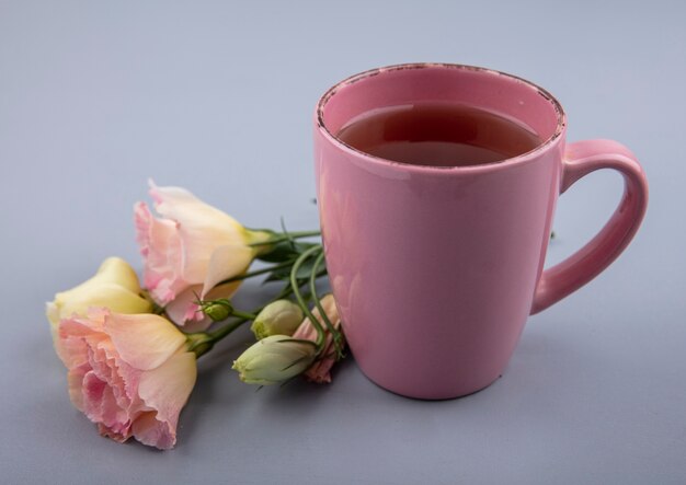 Vista superior de una taza de té rosa con flores frescas sobre un fondo gris
