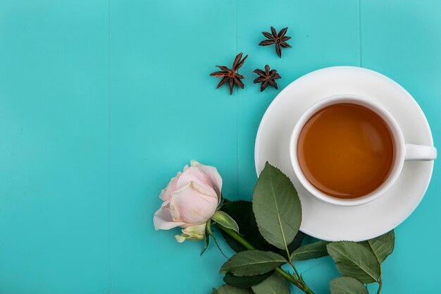 Vista superior de una taza de té con rosa fresca sobre un fondo azul con espacio de copia