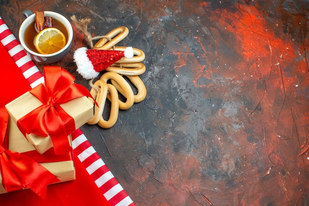 Vista superior taza de té con sabor a limón y canela mini gorro de Papá Noel sobre mantel rojo bagels ovalados en espacio libre de mesa rojo oscuro