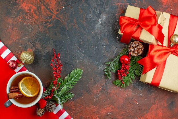 Vista superior taza de té con sabor a limón y canela regalos de ramas de árboles de Navidad en la mesa de color rojo oscuro