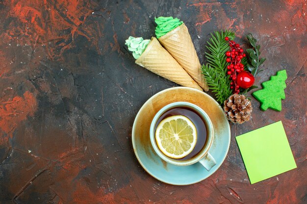 Vista superior taza de té con sabor a limón rama de árbol de navidad helados nota adhesiva en la mesa de color rojo oscuro con lugar libre