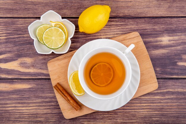 Vista superior de una taza de té en la tabla de cocina de madera con rodajas de limón con ramas de canela en madera