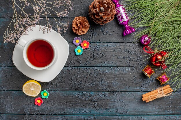 Vista superior de una taza de té una taza de té negro en el platillo blanco junto a las ramas de abeto de limón canela ramas con juguetes de Navidad y conos en la mesa