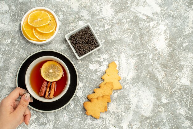 Vista superior de una taza de té en un tazón de galletas de mano de mujer con rodajas de chocolate y limón en el espacio libre de la superficie gris