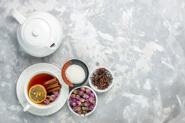 Vista superior de la taza de té con tetera y flores sobre la superficie blanca