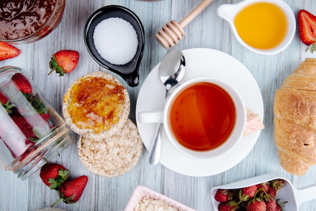 Vista superior de una taza de té con tortas de arroz miel fresas frescas azúcar y mermelada en rústico