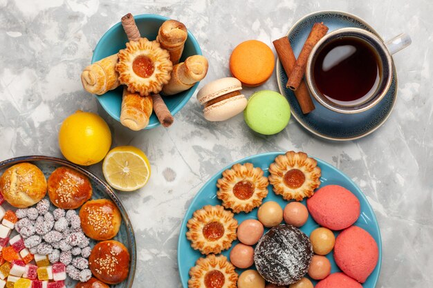 Vista superior de la taza de té con tortas, galletas y macarons en superficie blanca