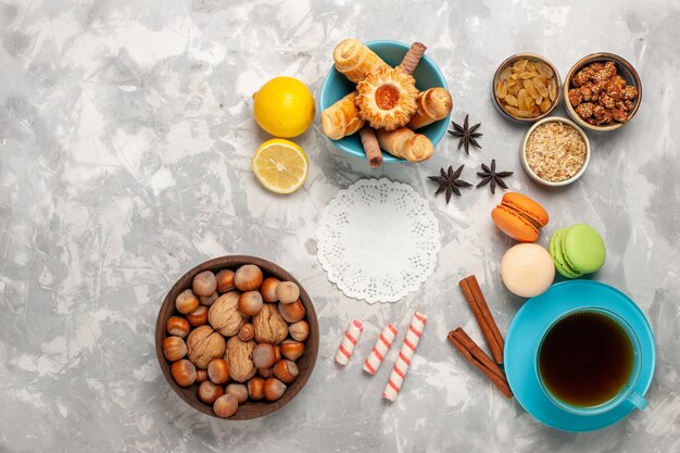 Vista superior de la taza de té con tortas y nueces sobre superficie blanca