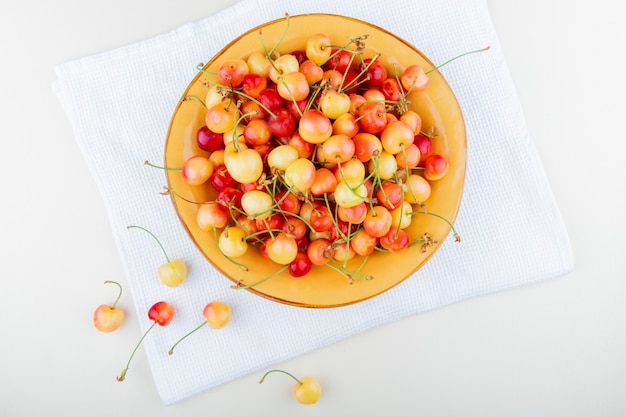 Foto gratuita vista superior del tazón con cerezas sobre tela y blanco