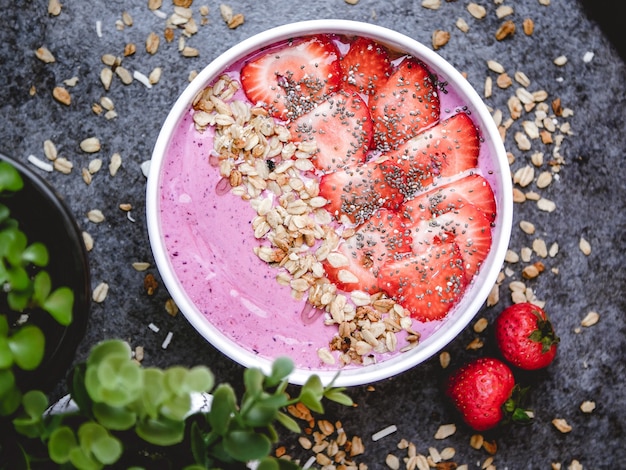 Vista superior de un tazón de desayuno saludable con yogur rosa, avena y fresas