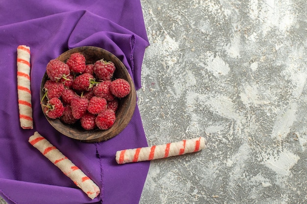 Foto gratuita vista superior de un tazón de frambuesas en una servilleta morada con galletas sobre un fondo de mármol