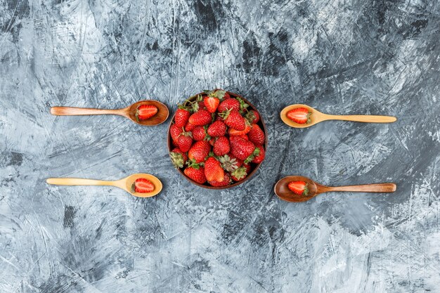 Vista superior de un tazón de fresas con cucharas de madera sobre la superficie de mármol azul oscuro.