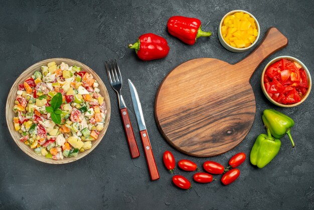 Vista superior del tazón de fuente de ensalada con verduras de cubiertos de soporte de placa sobre fondo gris oscuro