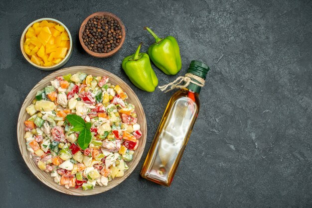 Vista superior del tazón de fuente de ensalada de verduras con tazones de verduras y botella de aceite de pimienta y pimientos en el lado sobre fondo gris