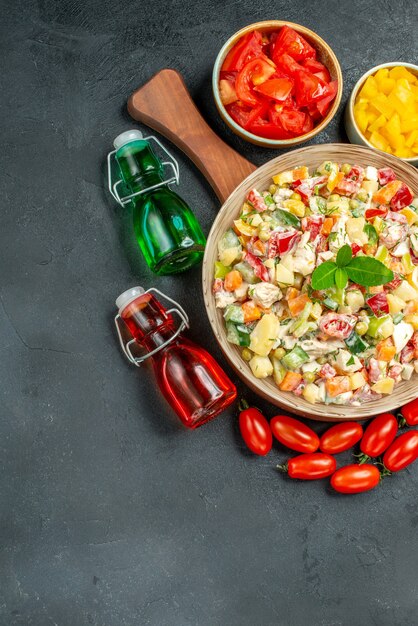 Vista superior del tazón de fuente de ensalada de verduras con verduras y botellas de vinagre de aceite en el lateral con espacio libre para el texto sobre fondo gris oscuro