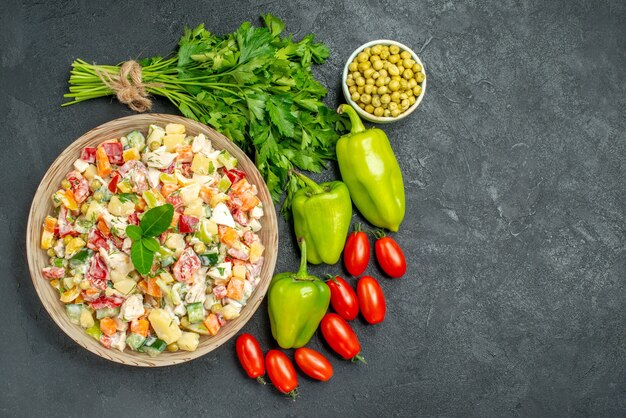 Vista superior del tazón de fuente de ensalada de verduras con verduras en el lado de la mesa verde oscuro