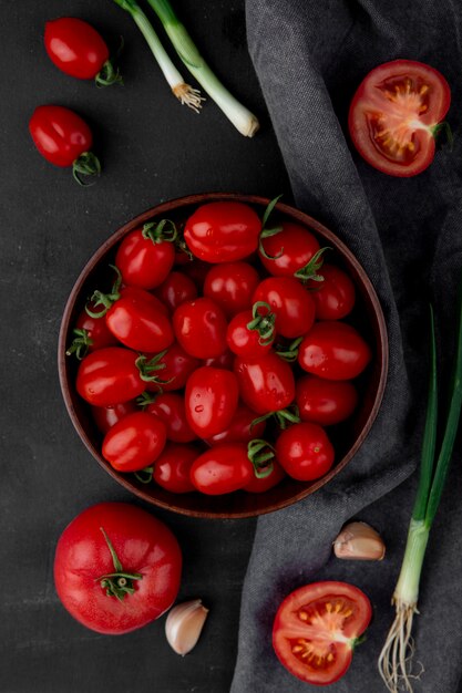 Vista superior del tazón lleno de tomates con otras verduras en superficie negra