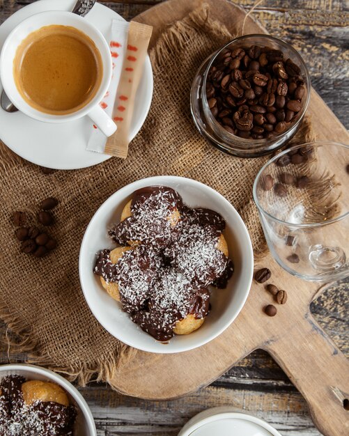 Vista superior del tazón profiterole cubierto con salsa de chocolate con chispitas de coco