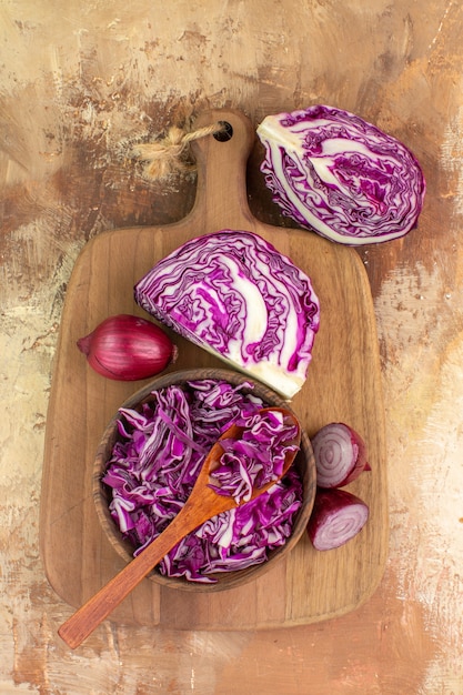 Foto gratuita vista superior de un tazón de repollo picado y algunas cebollas rojas sobre una tabla de cortar de madera para la preparación de ensalada de verduras en una mesa de madera con espacio de copia