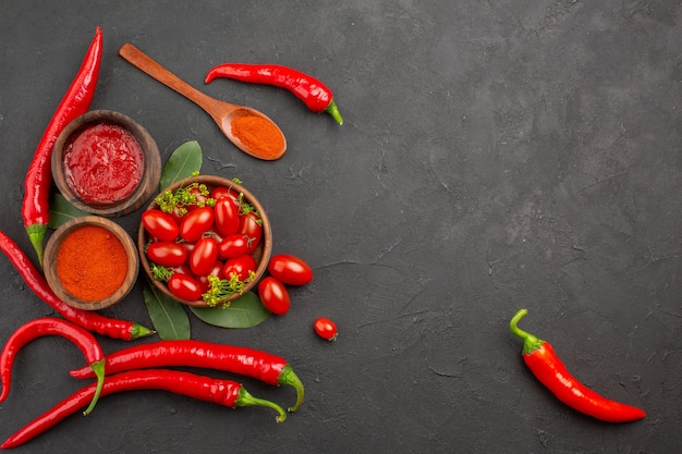 Vista superior de un tazón de tomates cherry pimientos rojos calientes una cuchara de madera hojas de laurel y tazones de salsa de tomate y pimiento picante en polvo sobre fondo negro