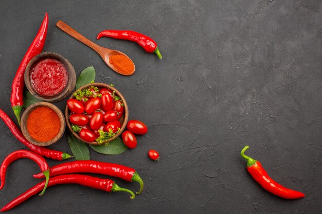 Vista superior de un tazón de tomates cherry pimientos rojos calientes una cuchara de madera hojas de laurel y tazones de salsa de tomate y pimiento picante en polvo sobre fondo negro