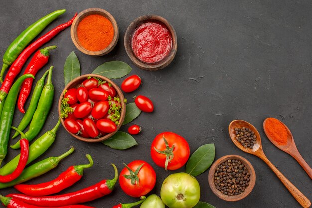 Vista superior de un tazón de tomates cherry pimientos rojos y verdes picantes hojas de laurel especias en cucharas de madera tazones de salsa de tomate pimiento rojo picante en polvo y pimienta negra y tomate en negro