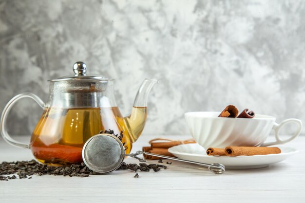 Vista superior de té de hierbas en una olla de vidrio y en una taza con limones canela sobre fondo blanco.