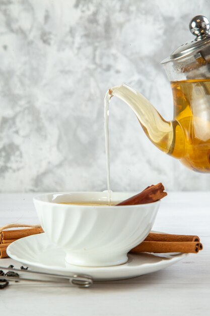 Vista superior del té de hierbas que se vierte de la olla en una taza sobre fondo blanco.