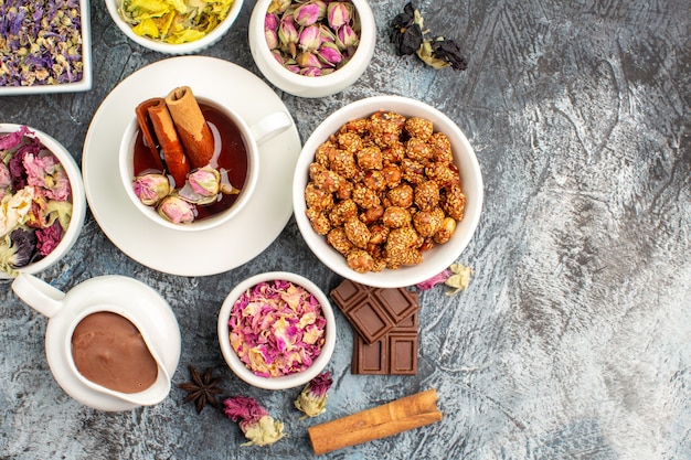 Foto gratuita vista superior de té de hierbas con un tazón de nueces y chocolate y diferentes tipos de flores sobre suelo gris