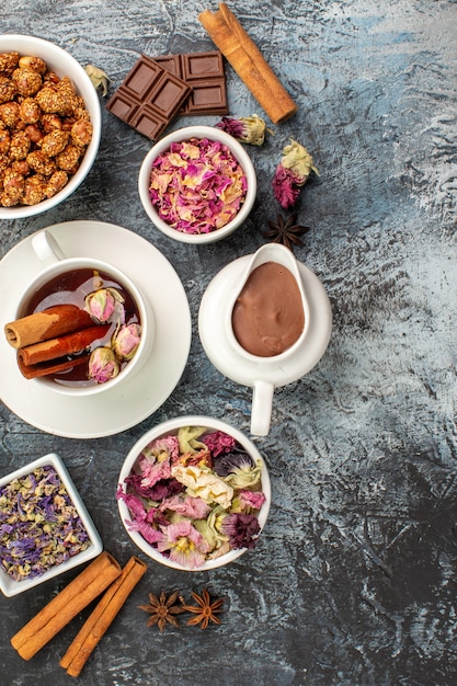 Vista superior de té de hierbas con un tazón de nueces y chocolate y flores secas sobre suelo gris