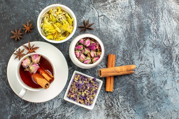 Vista superior de té de hierbas con tres tazones de flores secas y ramas de canela sobre fondo gris