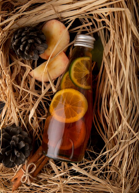 Vista superior de té de limón con canela en rodajas de manzana roja y cono de abeto en la paja