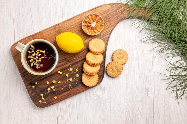 Vista superior de té y limón una taza de té con galletas de hierbas y limón en el tablero de la cocina y ramas de los árboles de Navidad