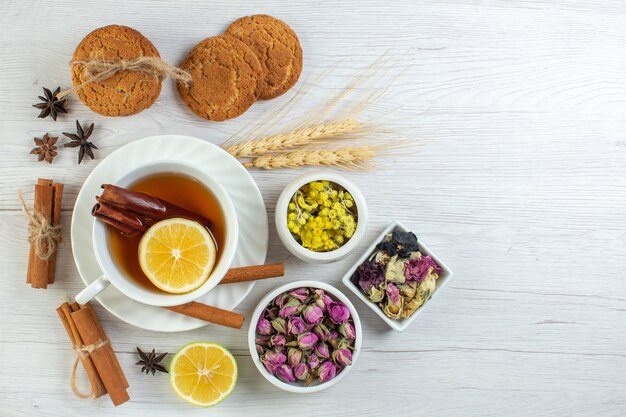 Vista superior de té negro con canela, limón, limón y varias galletas de hierbas en el lado derecho sobre fondo blanco.