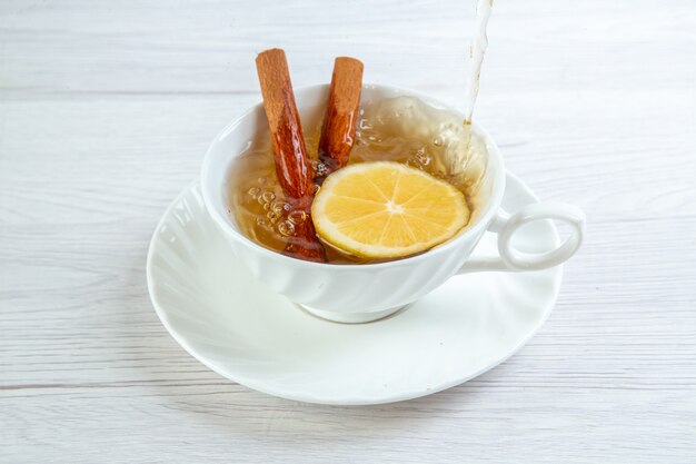 Vista superior de té negro con canela y limón en una taza blanca sobre mesa blanca