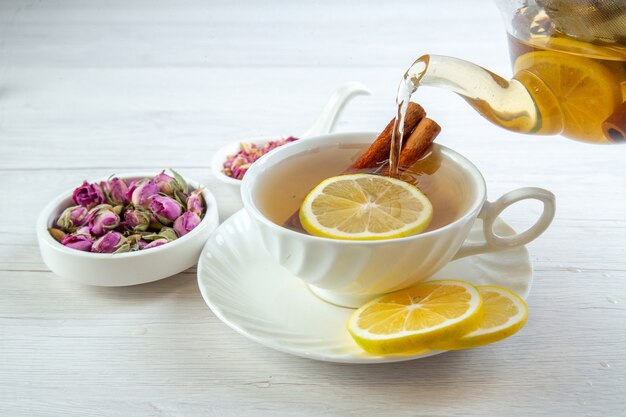 Vista superior de té negro con limas canela y limón en una taza blanca varios herbales sobre mesa blanca