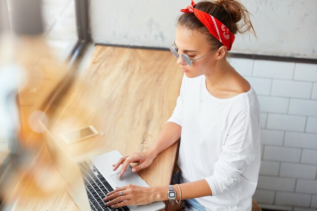 Vista superior de teclados femeninos jóvenes serios en netbook, funciona durante el desayuno de la mañana en la cafetería. Mujer redactora desarrolla servicios de marketing online, utiliza conexión a Internet de alta velocidad.