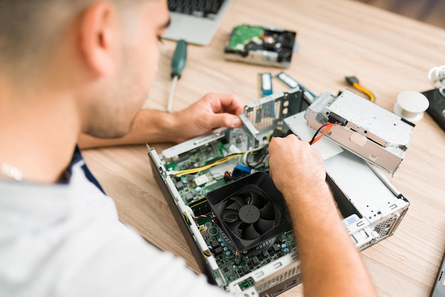 Vista superior de un técnico hispano arreglando el ventilador de la computadora. Joven conectando un nuevo componente en una CPU