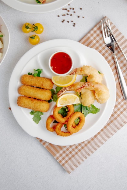 Vista superior de tempura de calamares y camarones y palitos de queso frito en un plato blanco