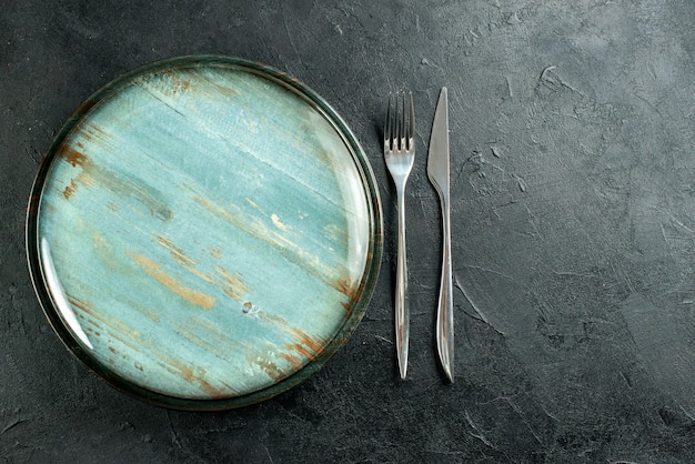 Vista superior del tenedor y el cuchillo de cena del plato redondo de acero en el lugar libre de la mesa negra